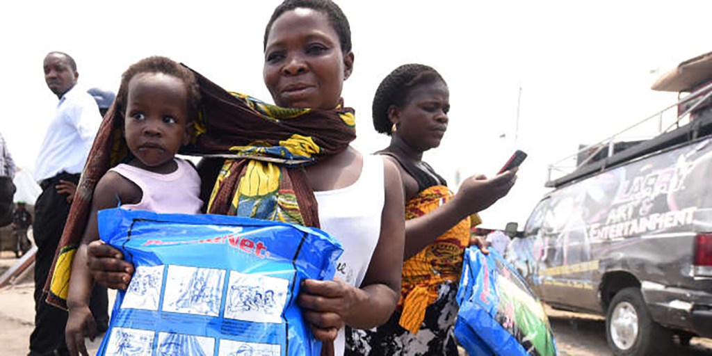 A woman carrying a baby holds a treated mosquito net during a malaria prevention action at Ajah in Eti Osa East district of Lagos, on April 21, 2016. - Dozens of patients and community members received malaria testing and treatment from the non-governmental organisation Development Africa, which in collaboration with Total company distributes treated mosquito nets and launches other actions to prevent malaria attacks to mark this year's World Malaria Day. (Photo by PIUS UTOMI EKPEI / AFP)